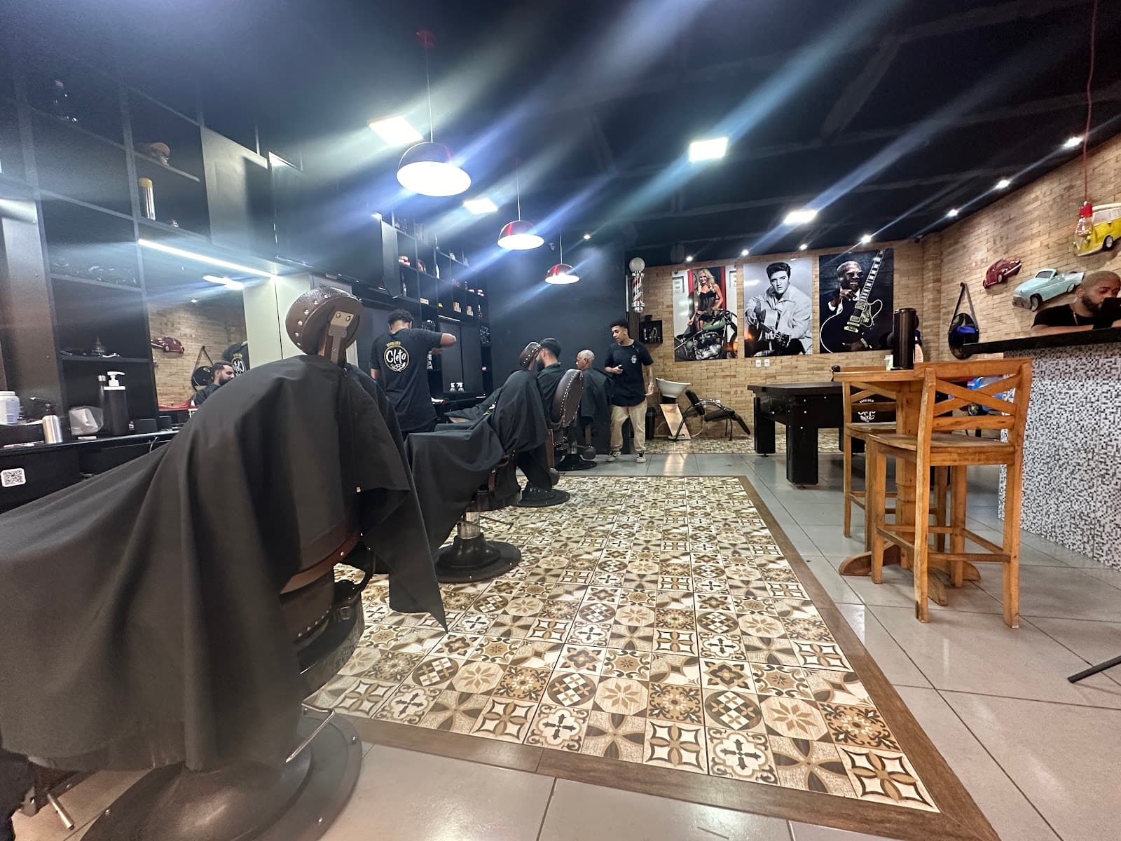Salão da Cleto visto da entrada: cadeiras de barbeiro, piso hidráulico, parede de tijolo e banquetas de madeira